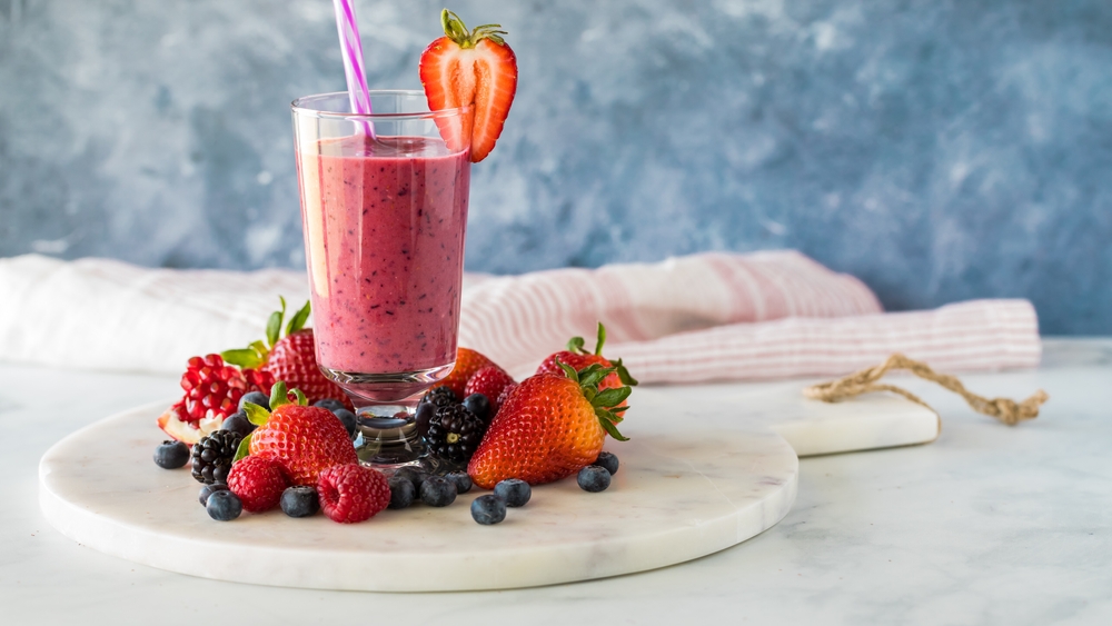 A mixed berry smoothie surrounded by fresh berries, ready for drinking.