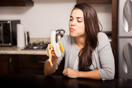 Healthy young woman eating a banana while sitting in the kitchen