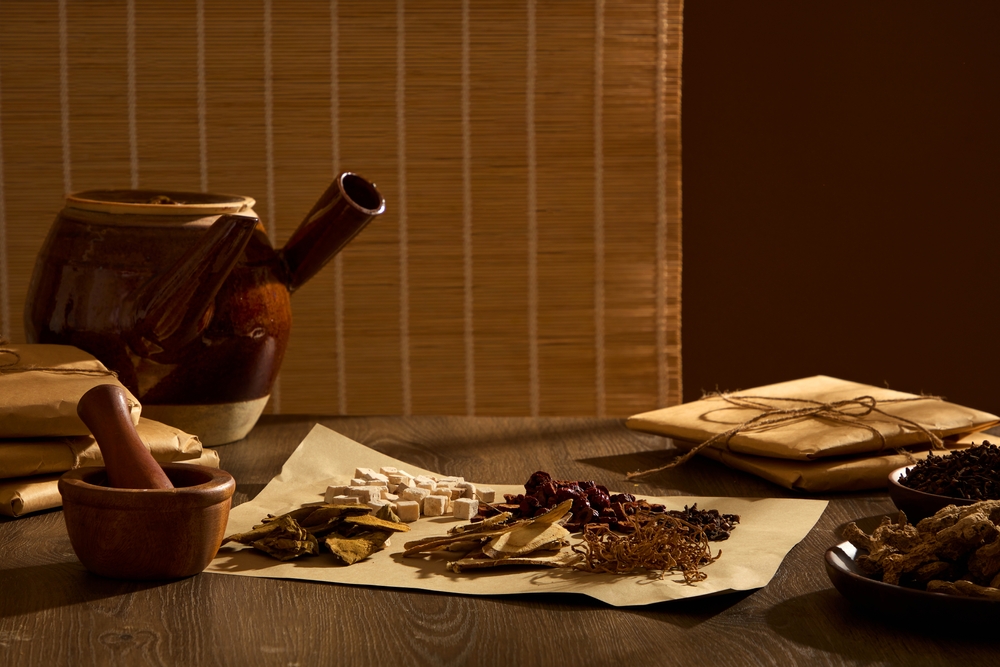 Concept of dividing herbs according to medicinal scale for daily intake. A medicinal kettle, and a sheet of paper containing various traditional medicines decorated on wooden table