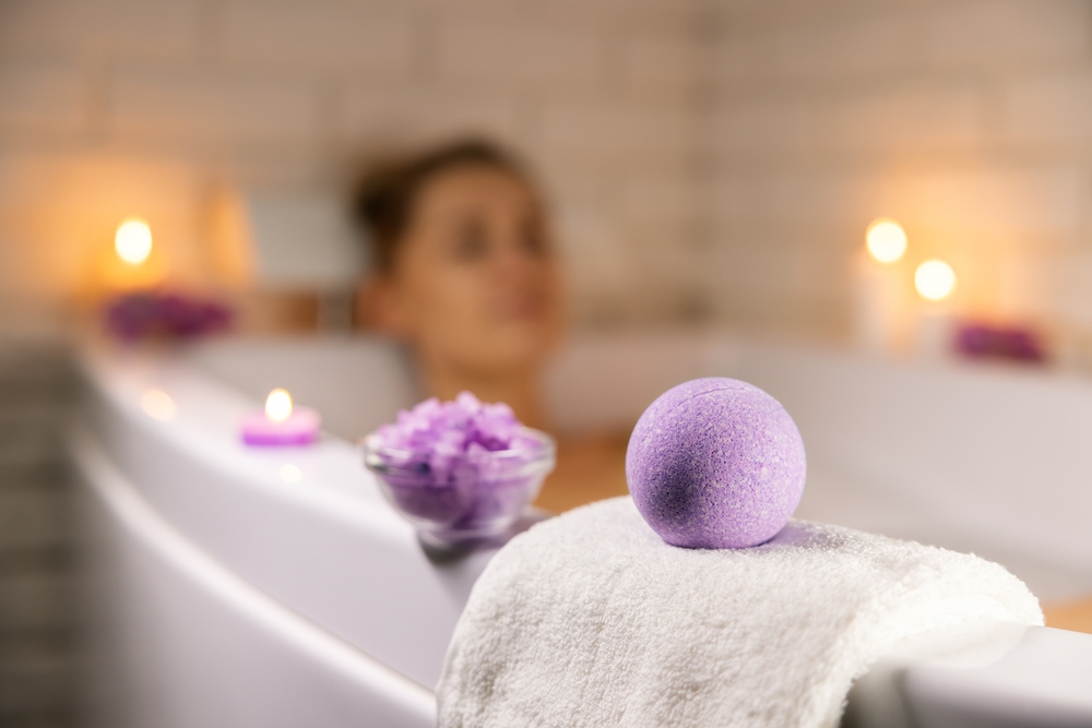 home spa. woman relaxing in bathtub in candle light and using bath bomb and sea salt crystals for body skin moisturizing
