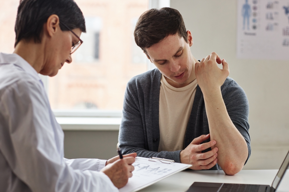 Portrait of young man showing skin rash to doctor during consultation in dermatology clinic
