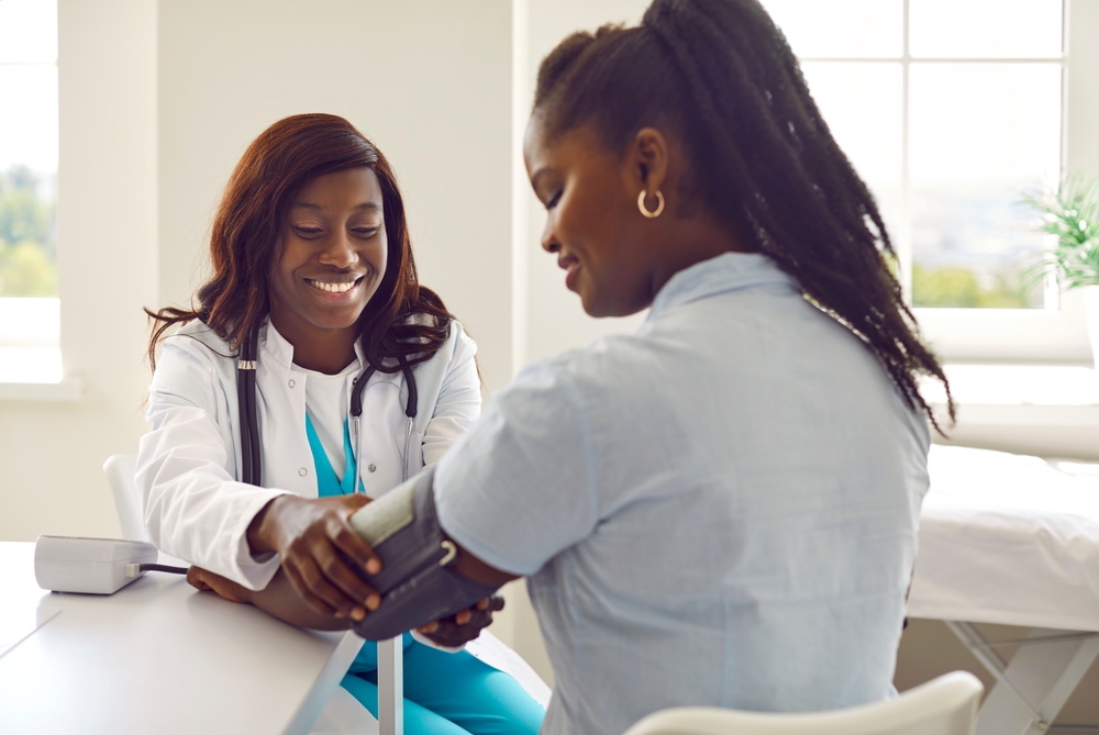 Smiling friendly african american woman doctor therapist measuring blood pressure of a young female patient in the office in clinic during medical examination. Healthcare and medicine concept.