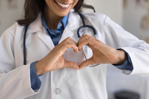 Cropped shot of young doctor woman showing hand heart, keeping romantic finger gesture at chest, expressing love, care, support for patients, early cardio disease diagnosing, checkup. Close up

