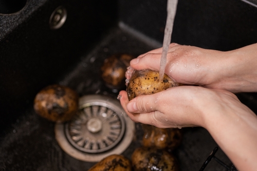 Hands holding and washing dirty potatoes over the sink. Preparing vegetables
