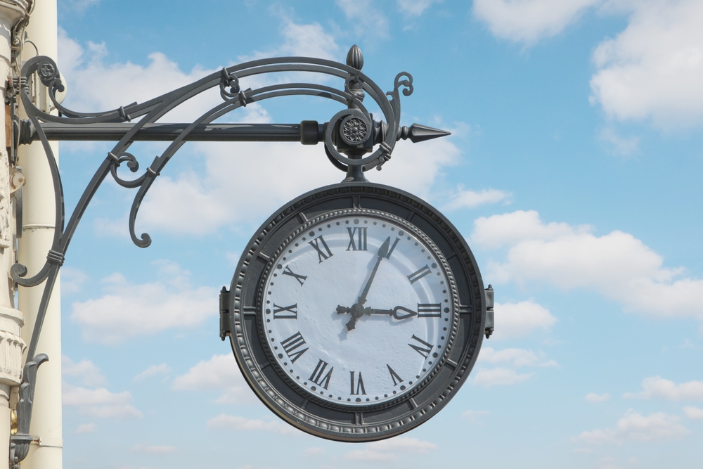 street clock on the wall of a building showing three hours, four minutes against a cloudy sky