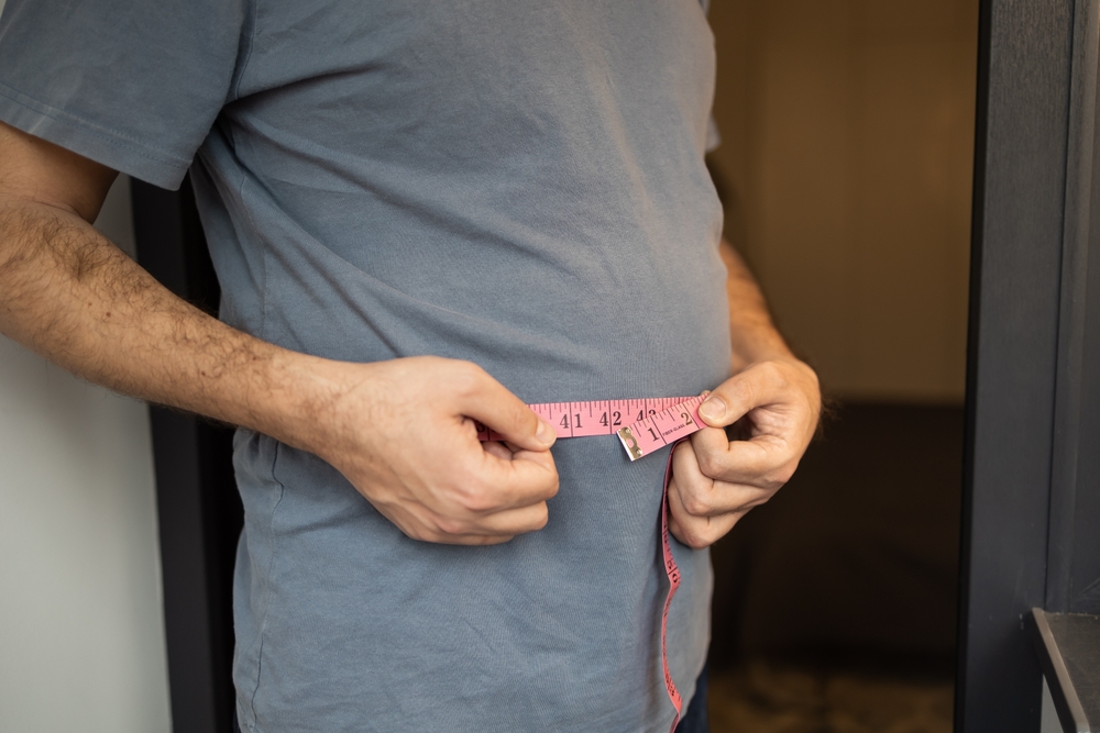 Overweight man measures his waist with measuring tape. Fat belly visceral fat. Body mass index, grade 1 obesity, eating disorders and physical activity, excess high-calorie food or eating disorder