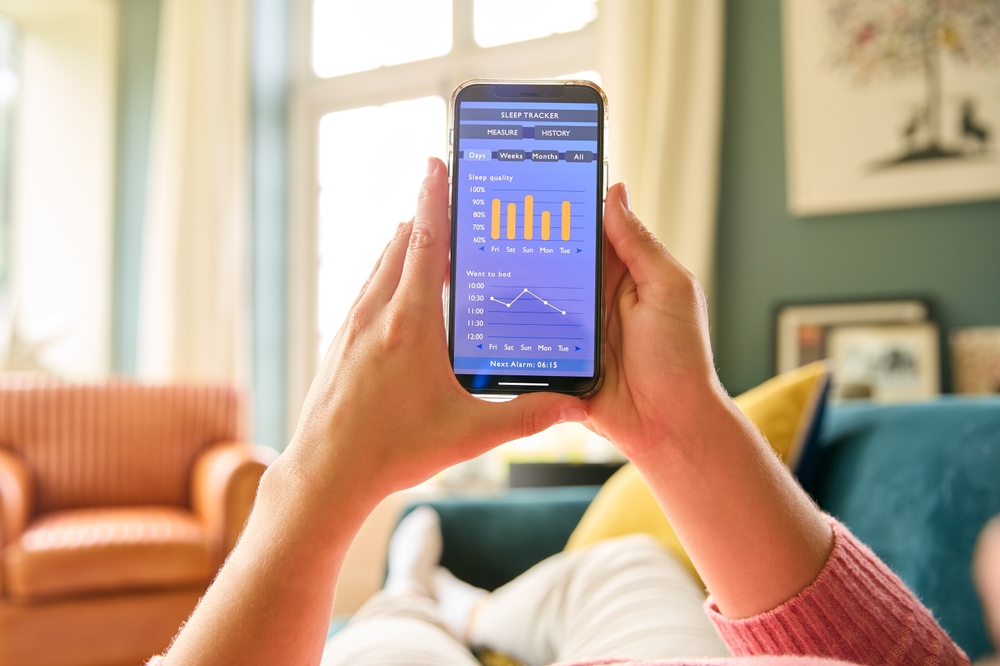 Close Up Of Woman Looking At Screen Of Sleep Tracker On Mobile Phone Relaxing On Sofa At Home
