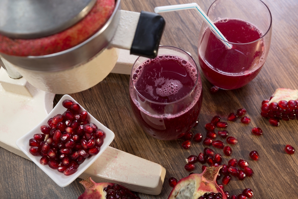 Freshly squeezed pomegranate juice in glasses and grains on the table