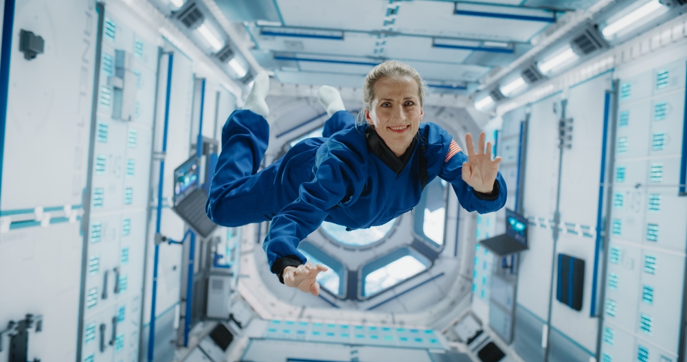 Portrait of a Courageous Caucasian Female Astronaut on Board a Spacecraft, Floating in Zero Gravity and Smiling At The Camera, Waving. Deep Space Travel, Solar System Exploration and Colonization.