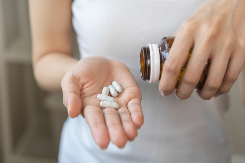 Dietary supplement or sick, asian young woman, girl hold pills, drugs medical tablet on hand pouring capsules from medication bottle, take vitamin for treatment for skin, hair at home, healthcare.
