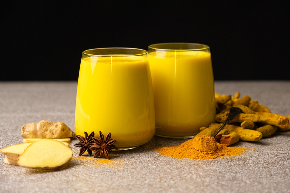 Golden milk, a traditional Ayurvedic drink with turmeric in two glasses on a black gray background.