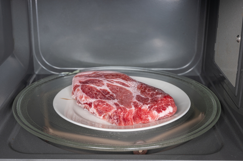 Raw pork in plate defrosting using microwave oven in close up