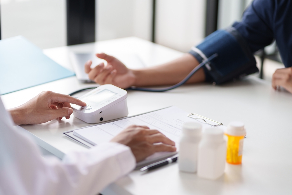 A doctor taking a patient's blood pressure. The patient's arm is equipped with a blood pressure cuff, and the doctor is using a blood pressure monitor.
