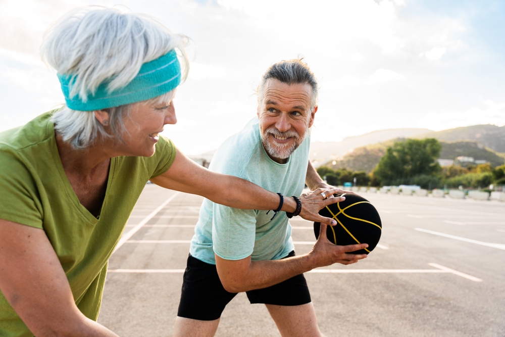 Beautiful happy senior couple playing basketball and having fun - Mature married couple in love bonding outdoors and doing sport together, concepts about elderly lifestyle, relationship and sports