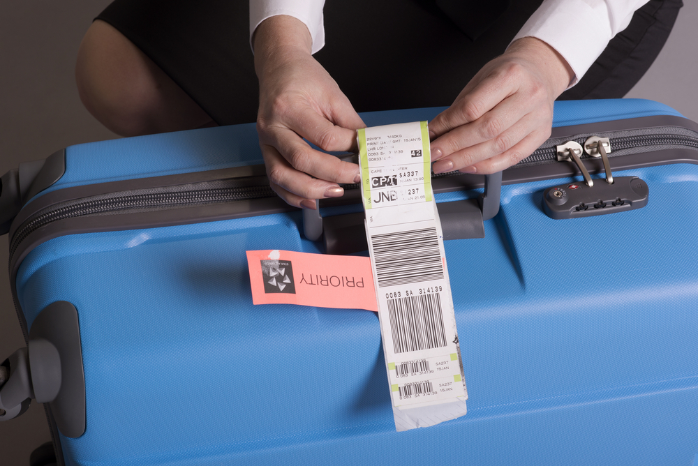 Airline check in luggage tag being attached to a suitcase. Priority tags