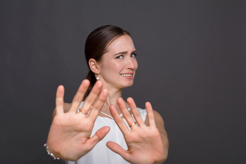 Attractive woman saying thanks but no. Beautiful girl denying proposal, making stop gesture with her hands, looking at camera