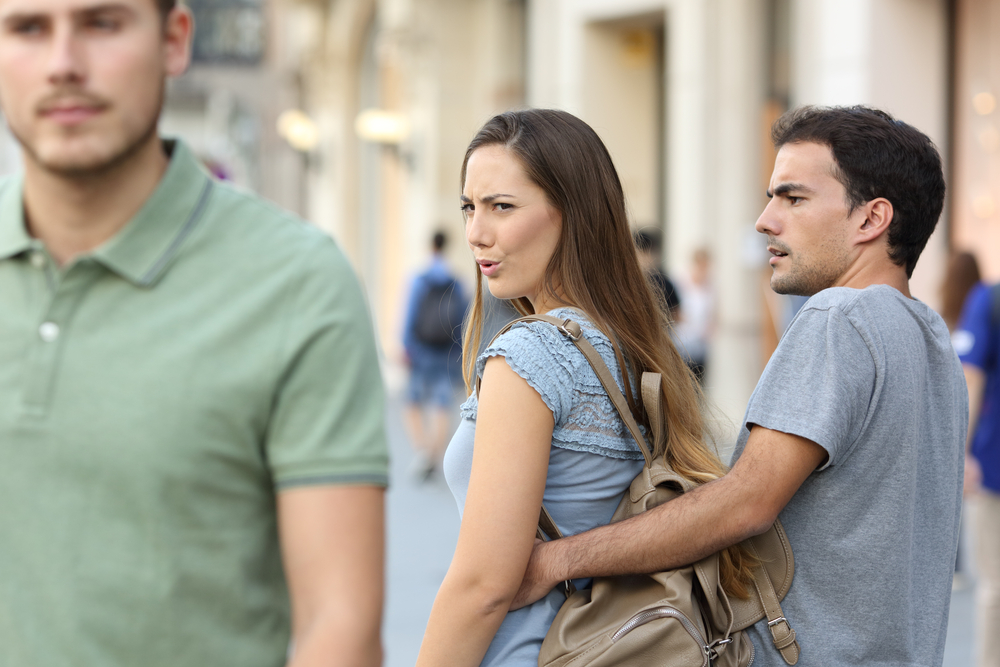 Disloyal woman looking another man and her angry boyfriend looking at her on the street