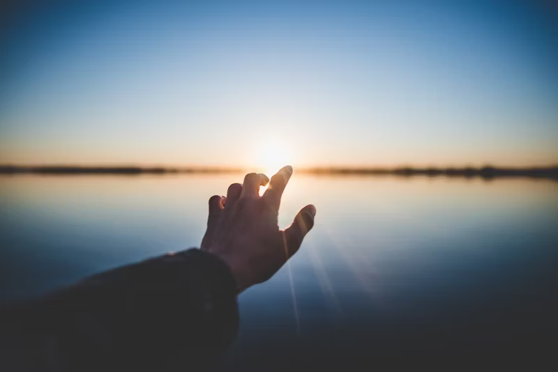 a hand reaching out towards the sun