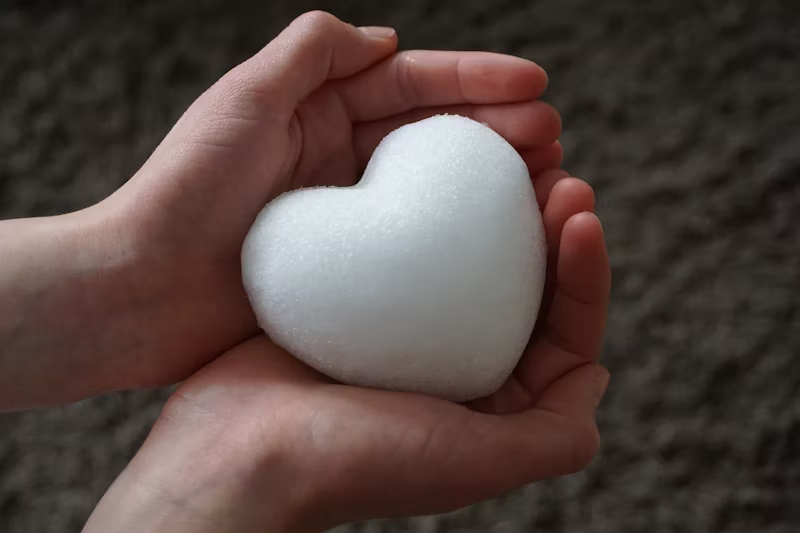 Bare hands holding a snow heart