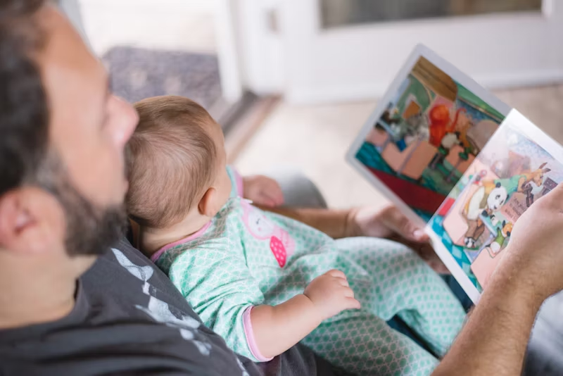A man and his son reading a book on the couch