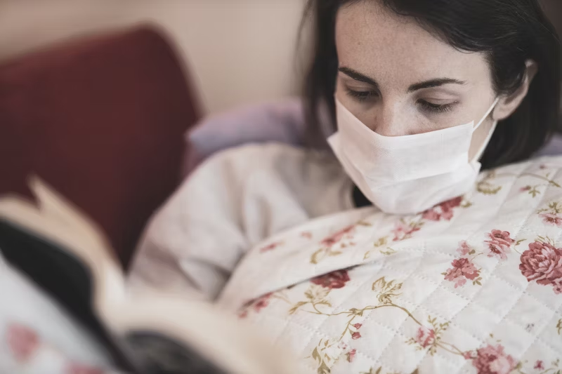 a woman reading a book with a face mask on