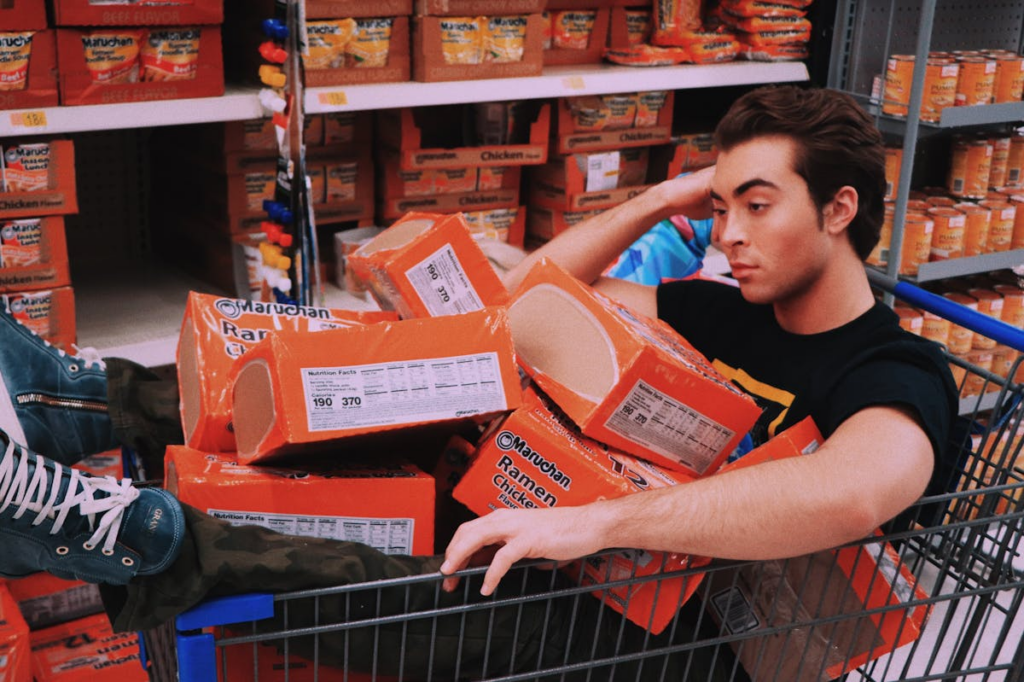 man in a grocery cart covered in ramen packets