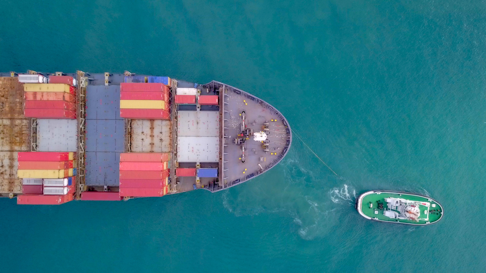 Large container ship pulled into port by a tugboat - Top down aerial image
