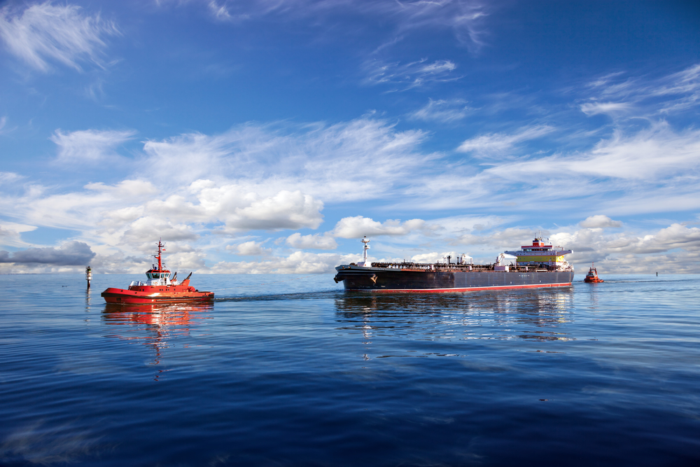 Tanker ship being guided into port by two tugs.
