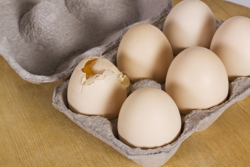Broken egg in a carton with other eggs