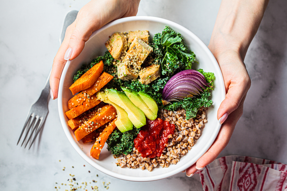 Baked vegetables, avocado, tofu and buckwheat buddha bowl. Vegan lunch salad with kale, baked sweet potato, tofu, buckwheat and avocado in a white bowl. Vegan concept.
