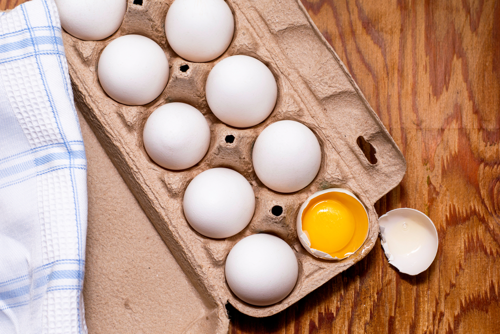 the broken egg with the yolk inside lies in the stand along with the whole eggs. High quality photo