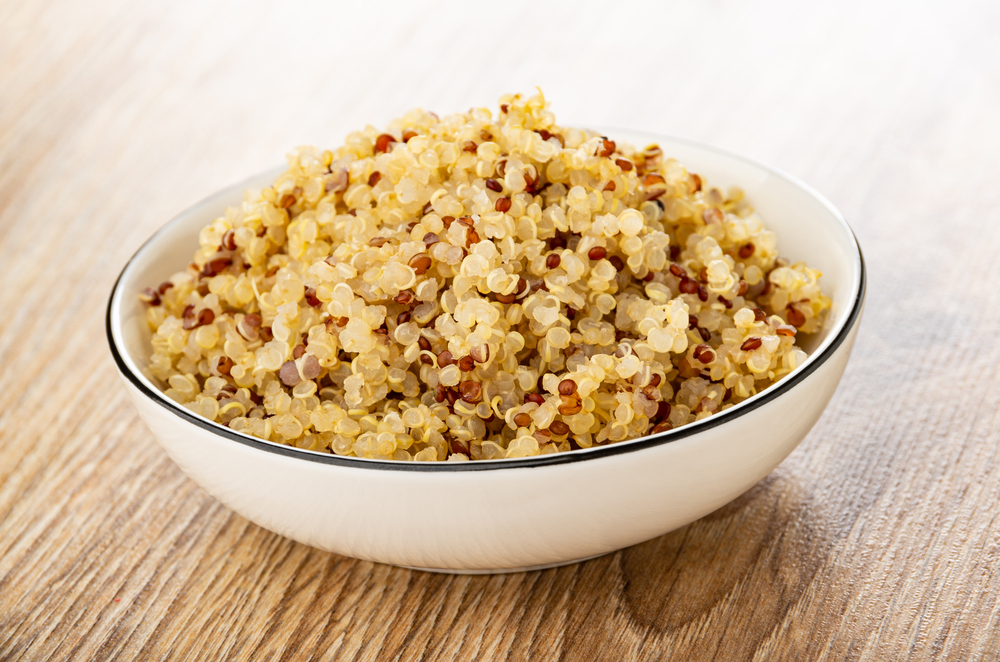 Boiled quinoa in white bowl on brown wooden table
