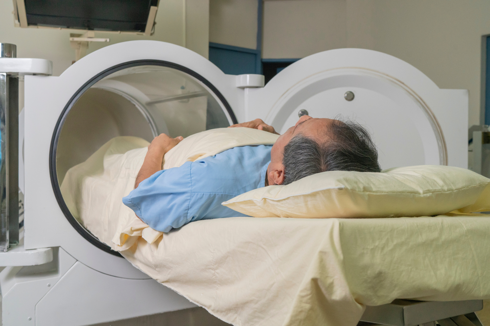 Older man lying on a stretcher starting treatment in the hyperbaric machine tube.
