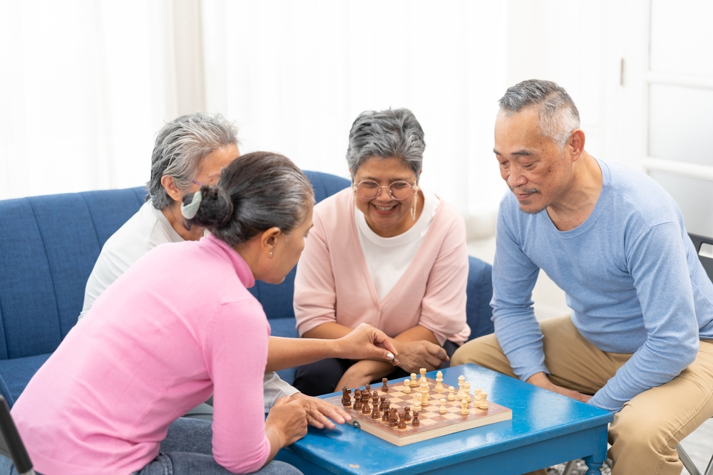 Asian senior people men and women in casual playing chess at nursing home, sitting around table. Asian Senior Elderly male spend leisure time. Happy smiling Older mature man enjoy activity in house.
