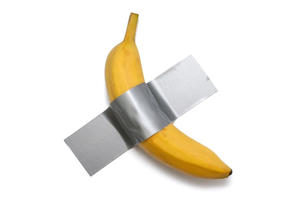 Banana taped with dact gray tape to a white wall. A conceptual look at contemporary art. Ripe banana duct taped to white isolated background
