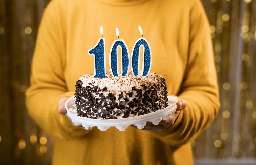 Woman holding birthday cake with number 100 candle, close up. One hundredth birthday or anniversary celebration. Copy space
