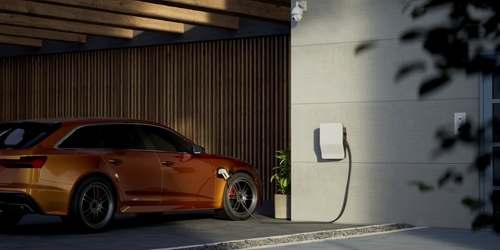 Generic electric vehicle EV hybrid car is being charged from a wallbox on a contemporary modern residential building house
