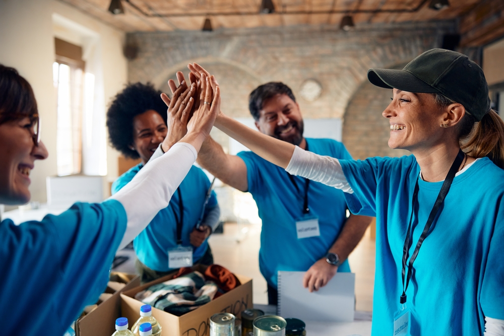 Group of happy volunteers gathering hands in unity while working at charitable foundation.

