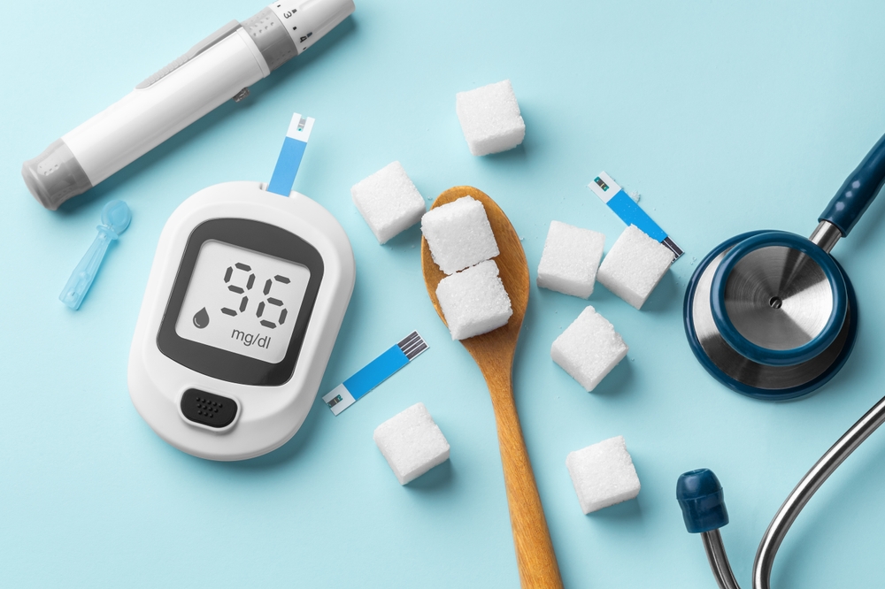 Diabetes concept with blood glucose meter, lancet and sugar cubes in spoon on blue background, top view