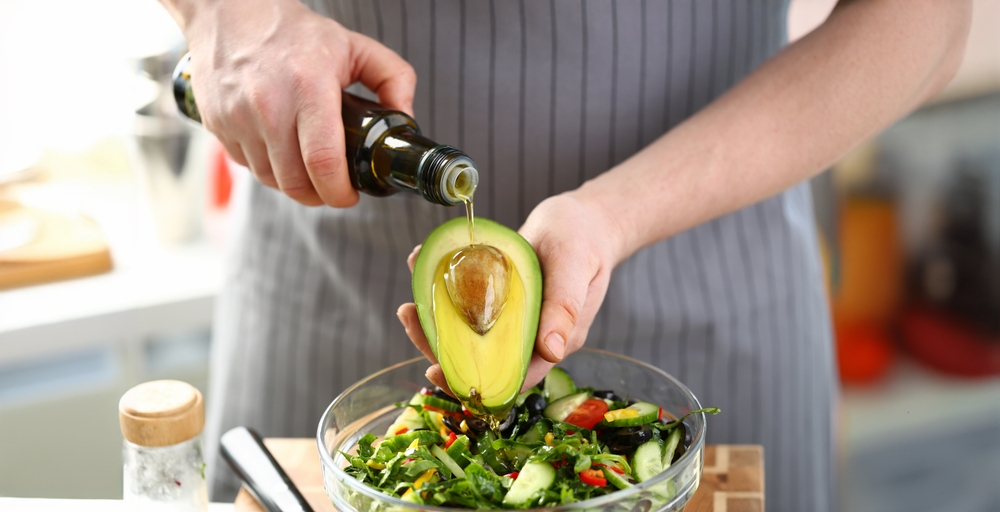Exotic Avocado Seed Ingredient Poured Olive Oil. Male Hands Holding Half Tropical Fruit. Chef Cooking Healthy Vegetable Salad with Greens, Cucumber and Tomato. Dieting Culinary Food Horizontal Photo
