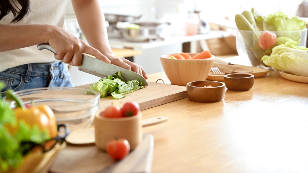 A close-up image of a woman cutting lettuces on a cutting board at a wooden kitchen tabletop, cooking in the kitchen. healthy food, lifestyle, home cooking