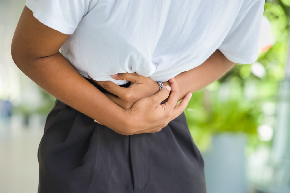 African woman with stomach ache, concept image of menstrual period cramp, abdominal pain, food poisoning, gastritis, acid reflux or colon cancer