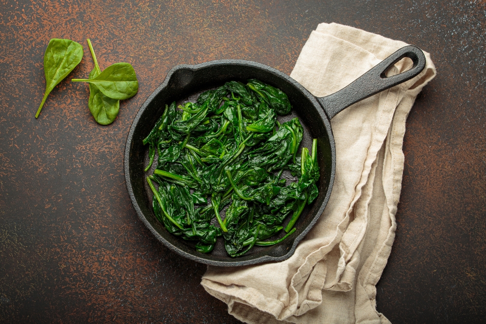 Healthy steamed spinach in cast iron pan on brown rustic background top view

