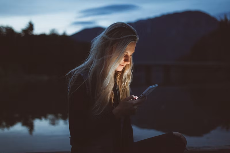 a woman outside with her face lit up by a phone screen