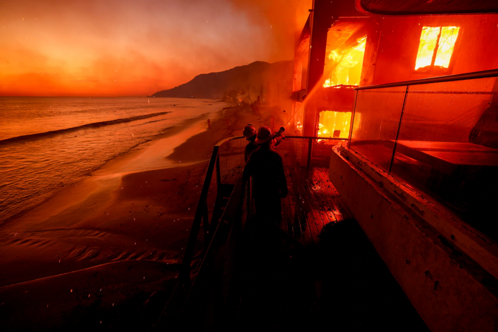 Firefighters work from a deck as the Palisades Fire burns a beachfront property. 