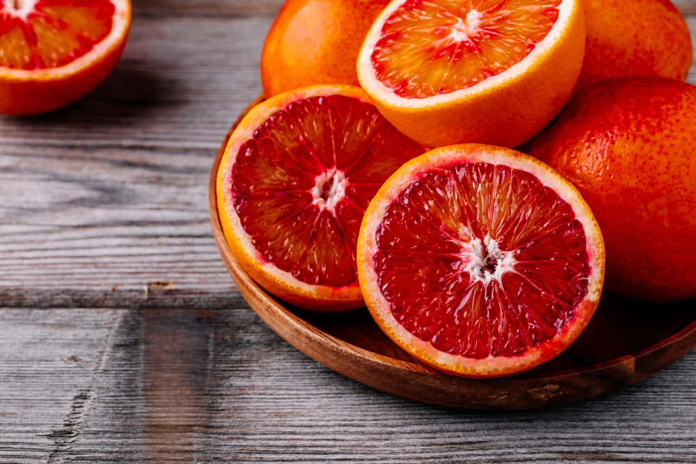 Sliced and whole ripe juicy Sicilian Blood oranges on wooden background. Selective focus