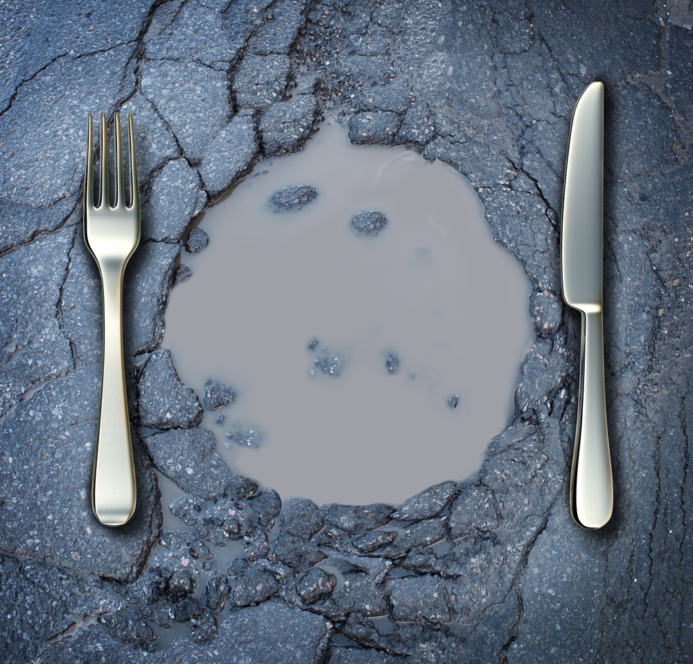 Poverty and hunger concept with a fork and knife on a broken asphalt road shaped as a dinner plate as a social crisis of food shortage hardships and living poor on the streets as a health risk.
