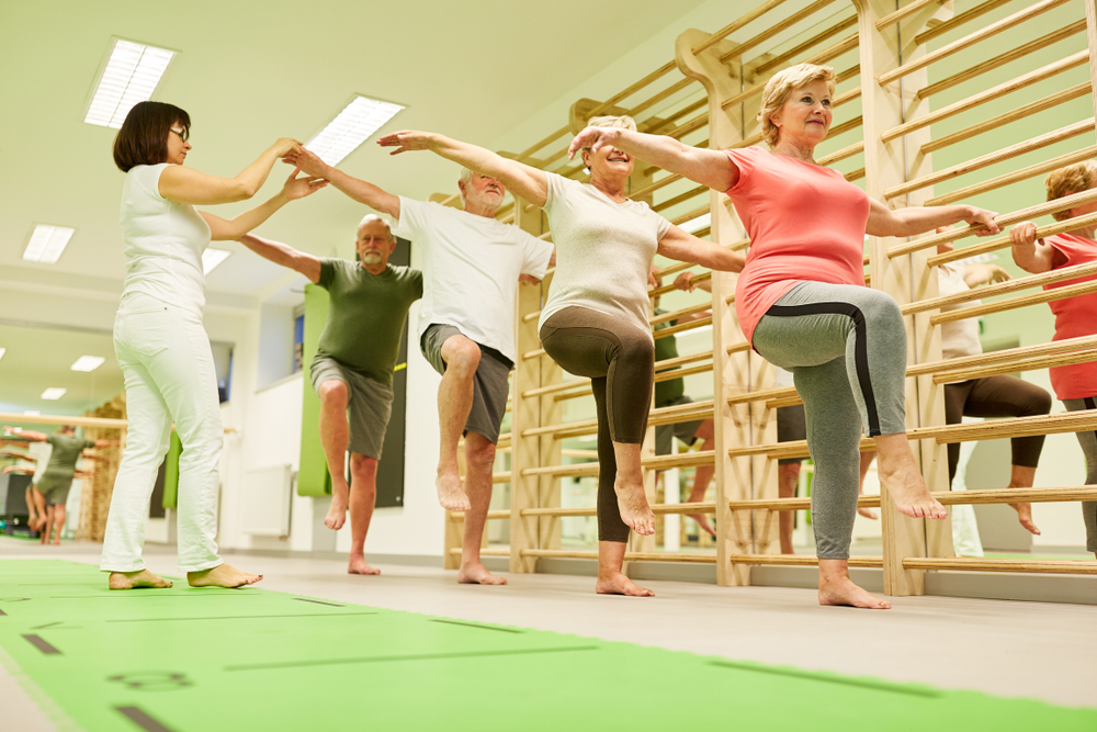 Physiotherapist supervises seniors group in gymnastics course with exercise on the wall bars