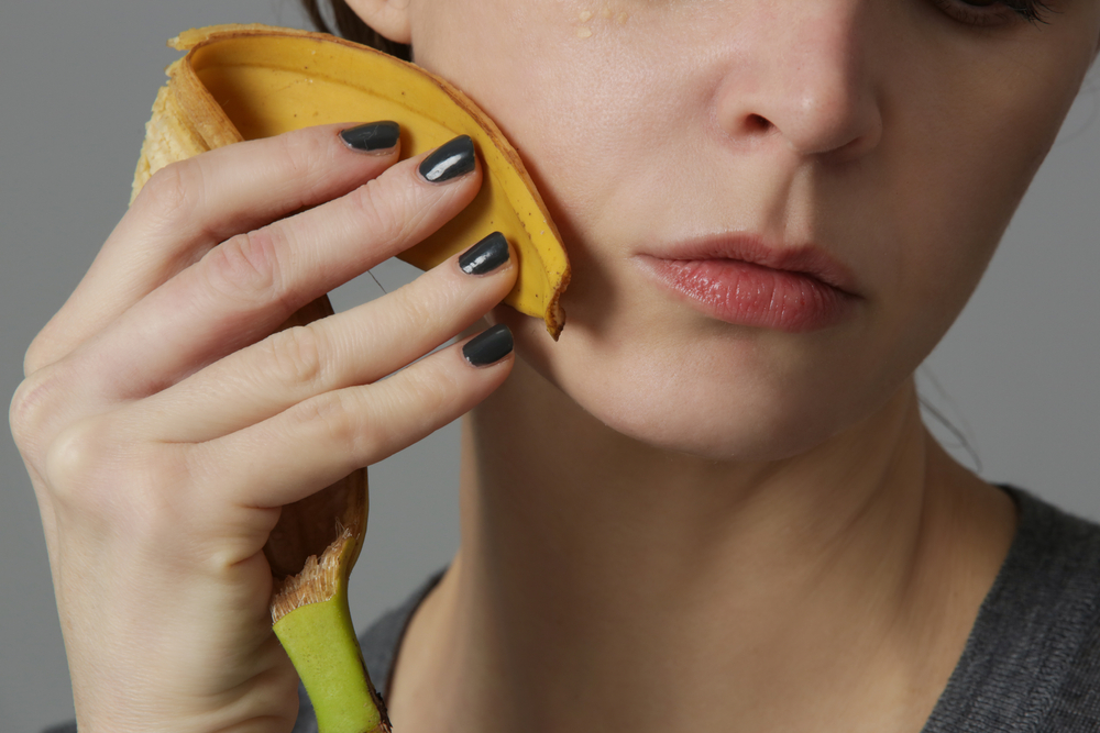 Woman rubbing banana peel on her face to brighten and hydrate skin and reduce wrinkles. Zero waste and natural skin care concept.
