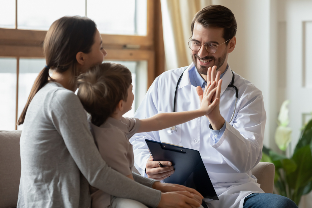 Happy male doctor have fun cheer support small 7s boy patient at visit to clinic with mom. Caring pediatrician give high five make deal with little child in hospital. Children healthcare concept.